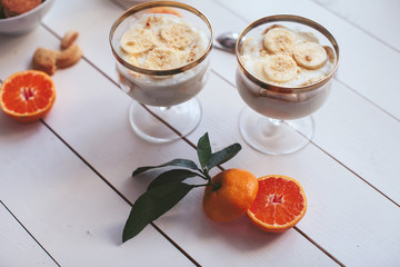 banana pudding with cookies in a cup on a white table with oranges and spoons