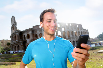 Happy male jogger listening music on smartphone against Colosseum. Smiling man is in sportswear....