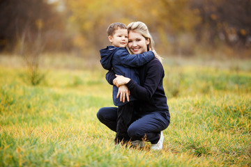 Naklejka na ściany i meble Young mother and son in autumn forest park, yellow foliage. Casual wear. Kid wearing blue jacket. Incomplete family, posing looking at camera positively. Childhood, children with parents are best
