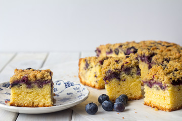 Slice of Blueberry Crumble Cake on a Plate on White Wooden Table with Copy Space