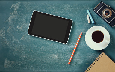 top view image of tablet, cup of coffee and photo camera over blackboard background
