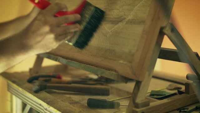 Adult man at work as artist, chiseling a bas-relief in his atelier. He brushes and cleans dust on a wood painting
