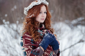 Portrait of attractive young redheaded woman. She is dressed in ethnic scarf and blue gloves. There is some snow in her hair. White wreath is on her head. She is praying.