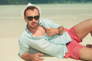 man lying down the beach with white hat and sunglasses on