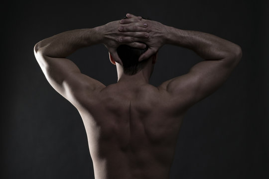 Handsome muscular bodybuilder posing on gray background. Low key studio shot