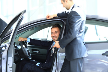 Young man choosing car at salon with help of consultant