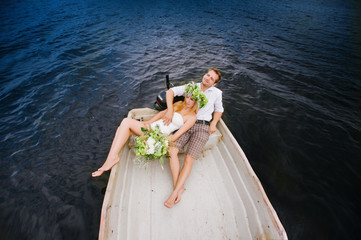 Happy young couple with a bouquet and a wreath hug sitting in a boat on the lake and sky background, lifestyle, love, relationships