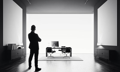 Businessman stands in modern office with two empty canvas. Black and white