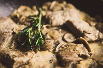 Grilled pork and mushrooms with cream sauce on the rustic background. Toned image.