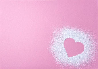 Heart shape made of icing sugar on pink grainy paper surface