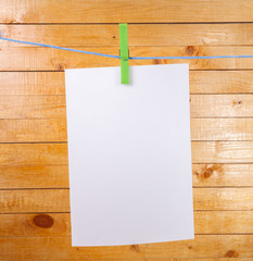 sheet of white paper hanging on clothespins on plank background