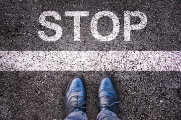Word Stop written on an asphalt road with legs and shoes