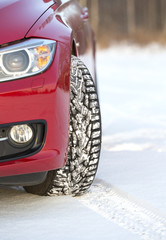 An image of a winter tyre covered with snow on an unidentified red car. Image taken during winter day in Finland.