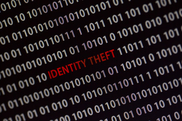 'Identity theft' text in the middle of the computer screen surrounded by numbers zero and one. Image is taken in a small angle.