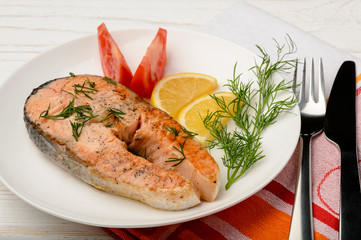 Roasted salmon, lemon and tomatoes on the white plate.