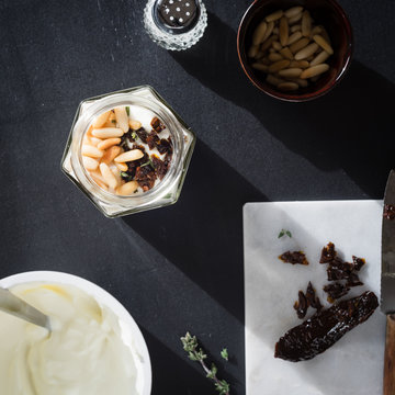 Greek yogurt with roasted pine nuts,  marinated dried tomatoes and thyme in jar on black background