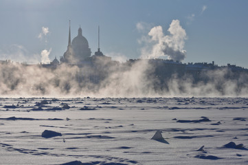 Very cold winter day in the city center of St. Petersburg. View of St. Isaac Cathedral and Admiralty building through the steam rising over ice channel to navigate the frozen Neva river. - 101034670