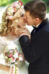 Beautiful happy young bride kissing handsome groom in sunlit par