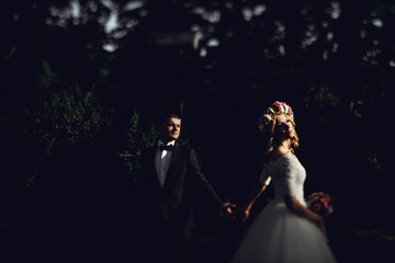 Romantic handsome groom in suit holding hands with gorgeous youn