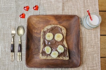 Chocolate spread on toast with sliced banana on a wooden plate with a glass of white milk