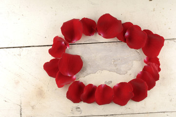 Frame of red rose petals on a wood background.
