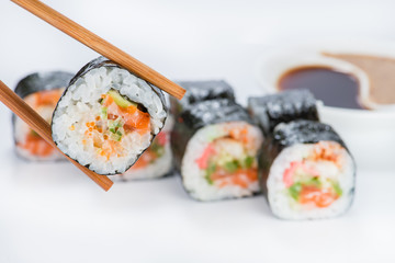 close up of chopsticks taking portion of sushi roll on the table