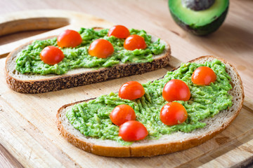 Guacamole and bread. Toast with avocado and cherry tomatoes on wooden cutting board