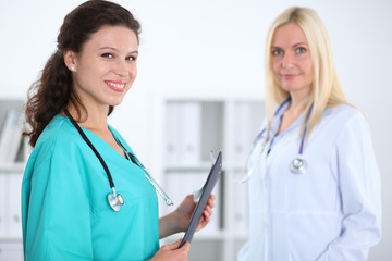 Fototapeta premium Two confident friendly female doctors sitting at the table and listen to the patient's history . Medical and health care concept