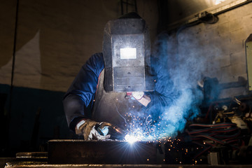 Manufacture worker welding metal at factory workshop with flying sparks