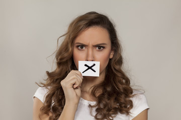 angry young girl with X sign drawn on paper over her mouth