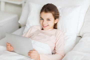 happy girl lying in bed with tablet pc at home