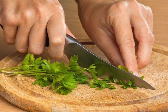 hands chopping parsley leaves on the wooden cutting board