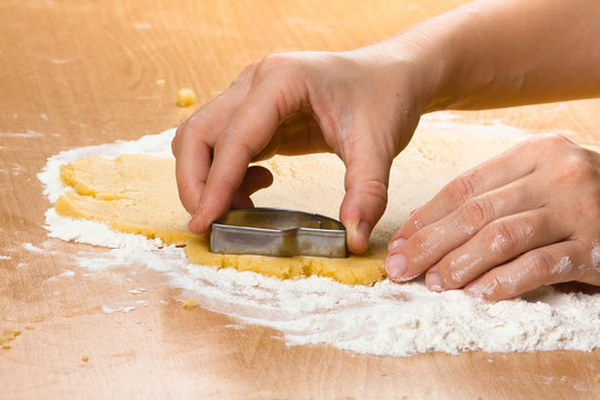 hands cutting cookies from the dough with metal cutter