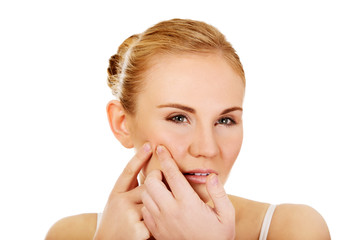 Unhappy young woman squeezing pimple on face