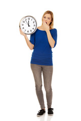 Young yawning woman holding a clock