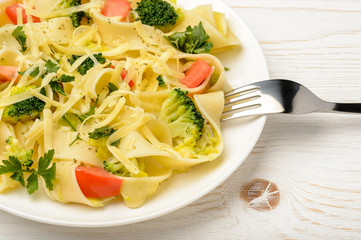 Italian pasta with broccoli, tomatoes and cheese on wooden table.