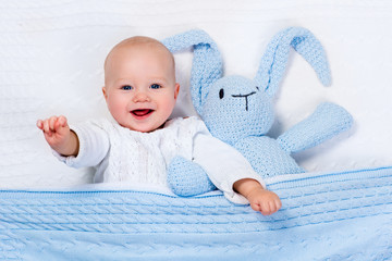 Baby boy playing with blue knitted bunny toy - Powered by Adobe