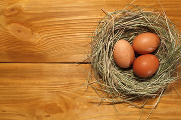 The composition of chicken eggs lying in a nest of grass on a panel of vintage brown boards with free space for text advertising of food or restaurant menu design.