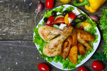 roasted chicken legs with potatoes with Greek salad on wooden background with vegetables