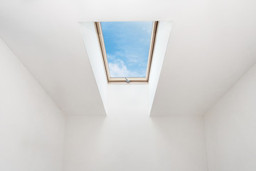 A modern open skylight (mansard window) in an attic room against blue sky