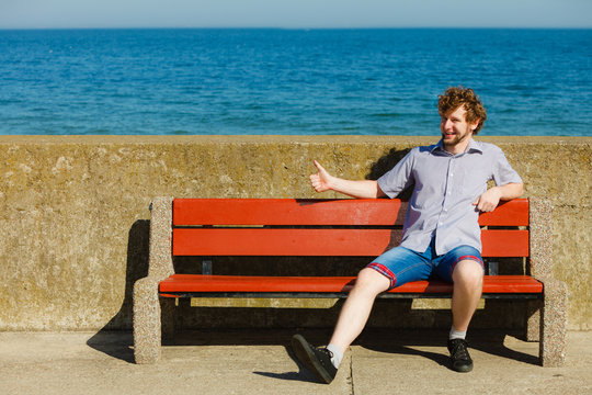 Happy young man sitting on bench by sea ocean.