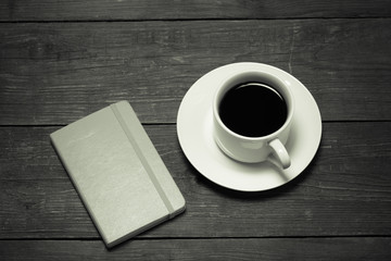 White cup of coffee and notebook on old wooden table. Toned