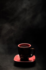 A cup of coffee with smoke on black background. Toned