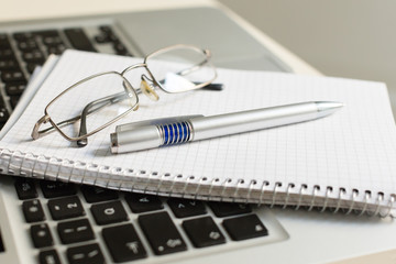 Laptop computer with notepad, pen, glasses and keyboard
