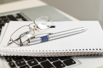 Laptop computer with notepad, pen, glasses and keyboard