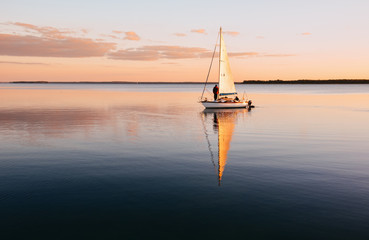 Sailing boat on a calm lake with reflection in the water. Serene scene landscape.