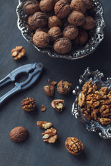 Walnuts in a bowl, whole and chopped on grey wooden table. Vintage style
