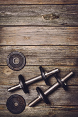 Old iron dumbbells with extra plates on an old wooden table. Image taken from above, top view. 