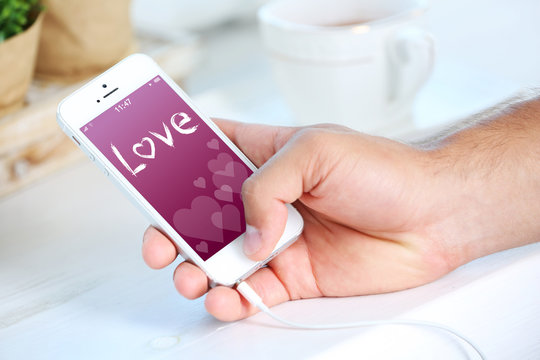 Smartphone with romantic screensaver in male hand, on light background
