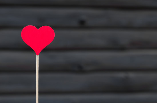 Red heart on stick against a dark wood background.